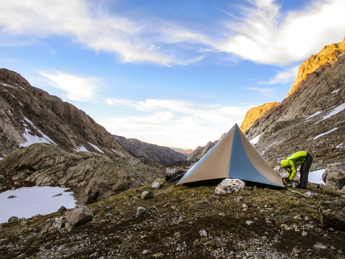 A person adjusts a tent string in a rocky mountain valley