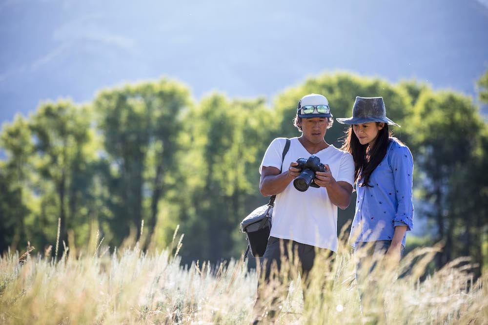 Jimmy Chin and Elizabeth Chai Vasarhelyi look at camera while standing in field bounded by trees