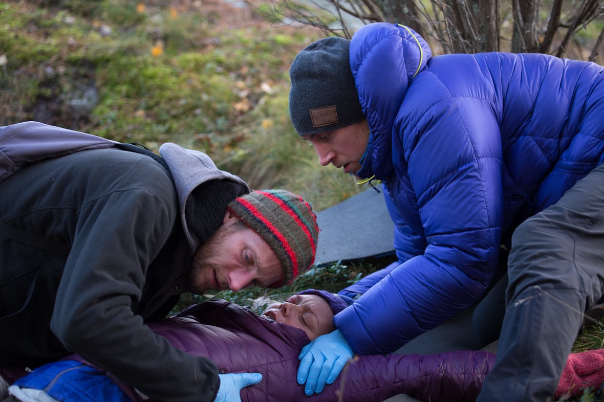 two NOLS wilderness medicine students wearing warm clothing practice caring for a patient lying on the ground outside