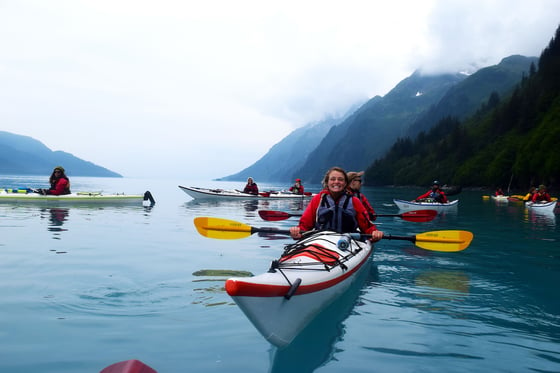 NOLS participants in single and double kayaks float on calm water on a foggy day in Alaska