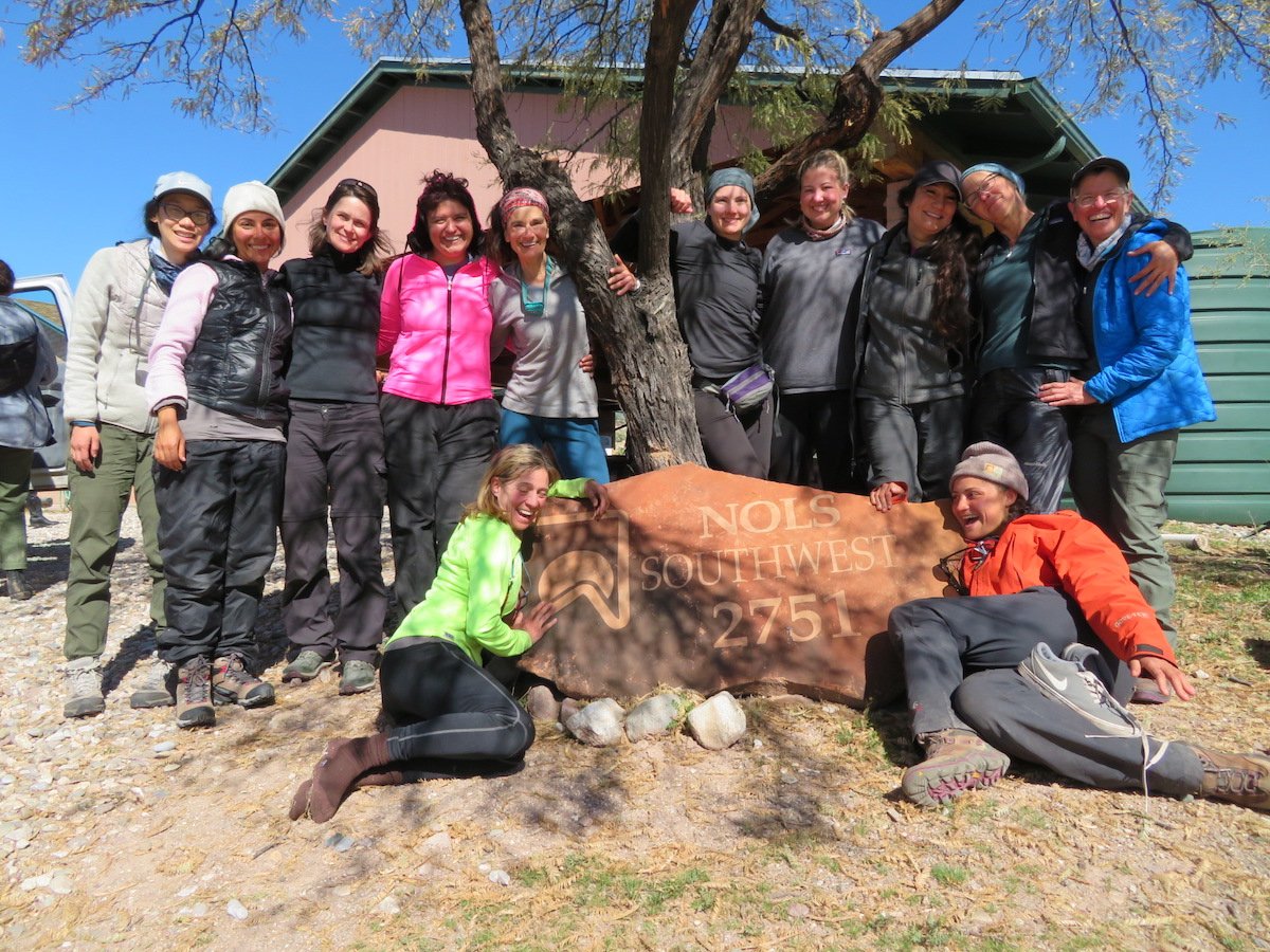 Group of women smiles in front of the NOLS Southwest address marker