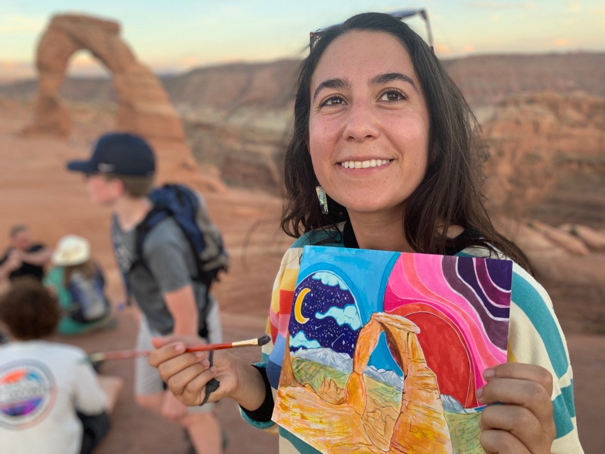Artist smiles and holds up a painting of redrock arch