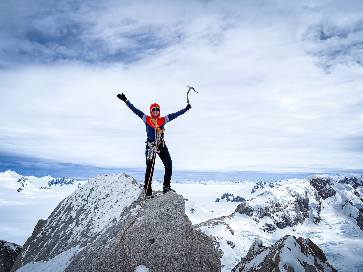 Woman stands on the summit and lifts her arms in celebration