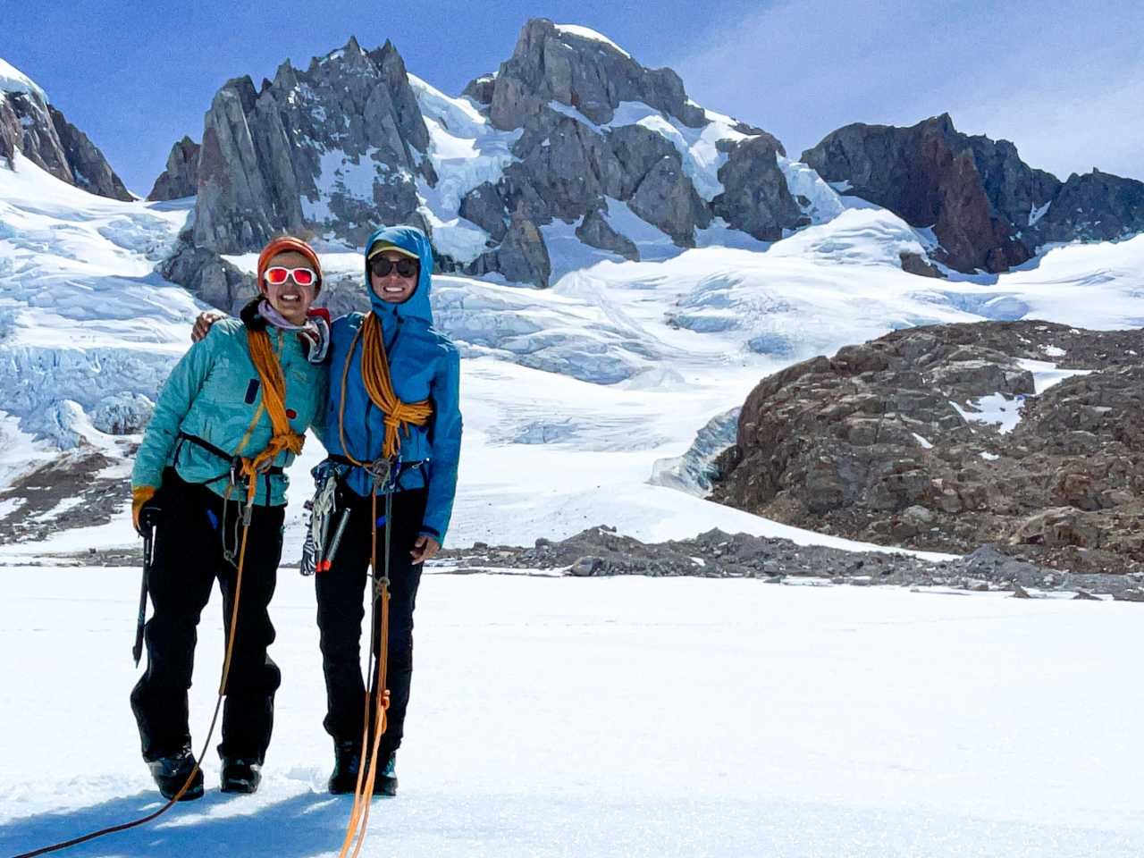Two women smile while set up for glacier travel in front of Patagonian peaks