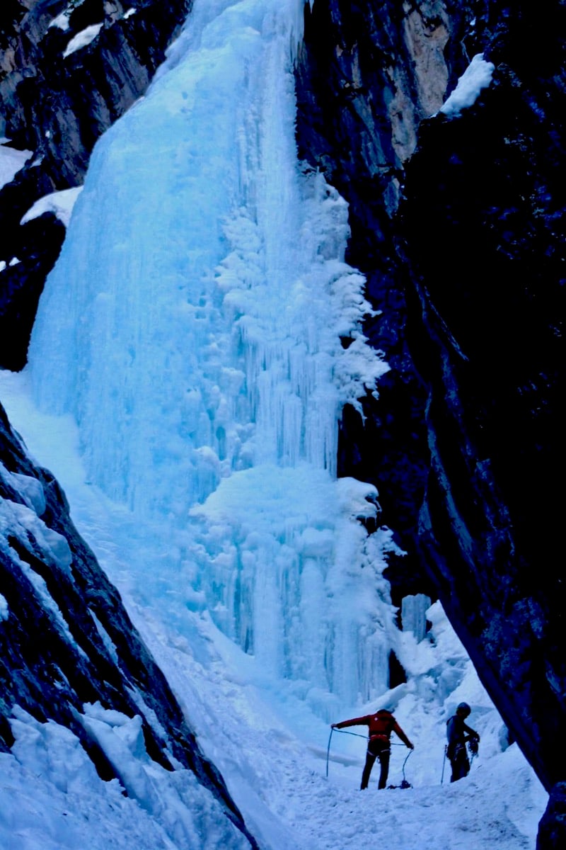Two climbers coil a rope at the base of an ice waterfall