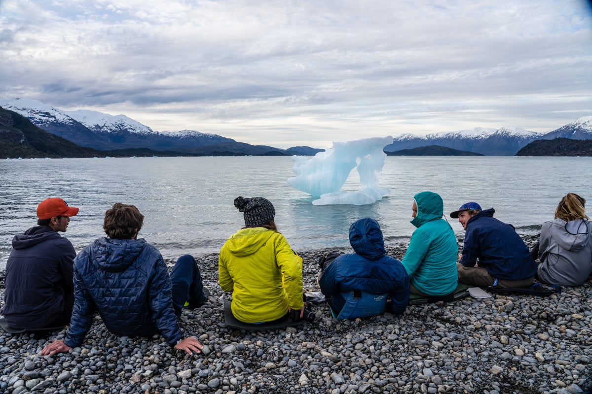 NOLS students sit on a rocky shore looking at a small ice floe