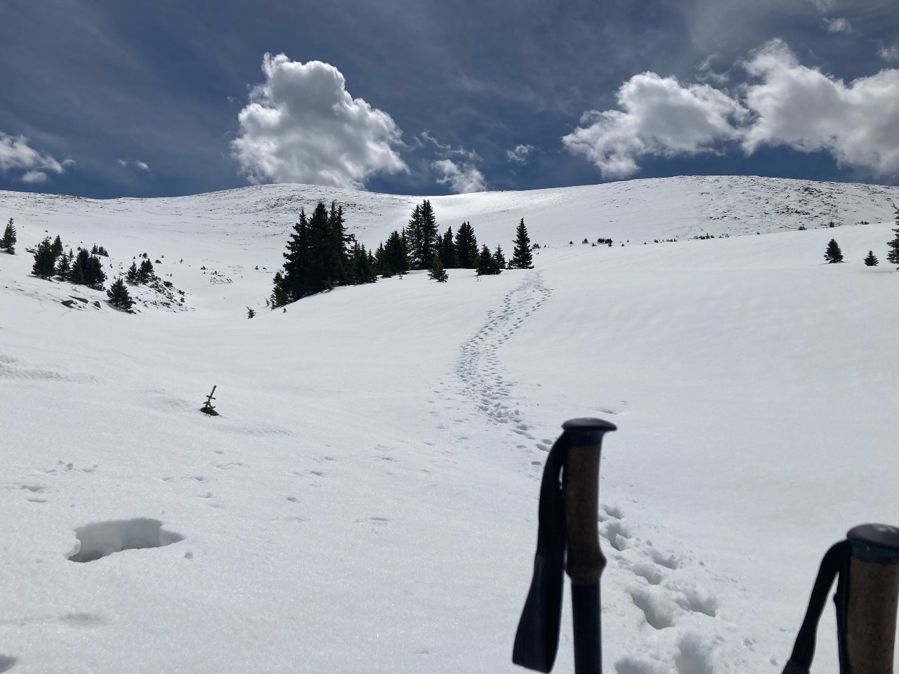 Snowy peak with footprints leading out of sight and ski poles in the foreground