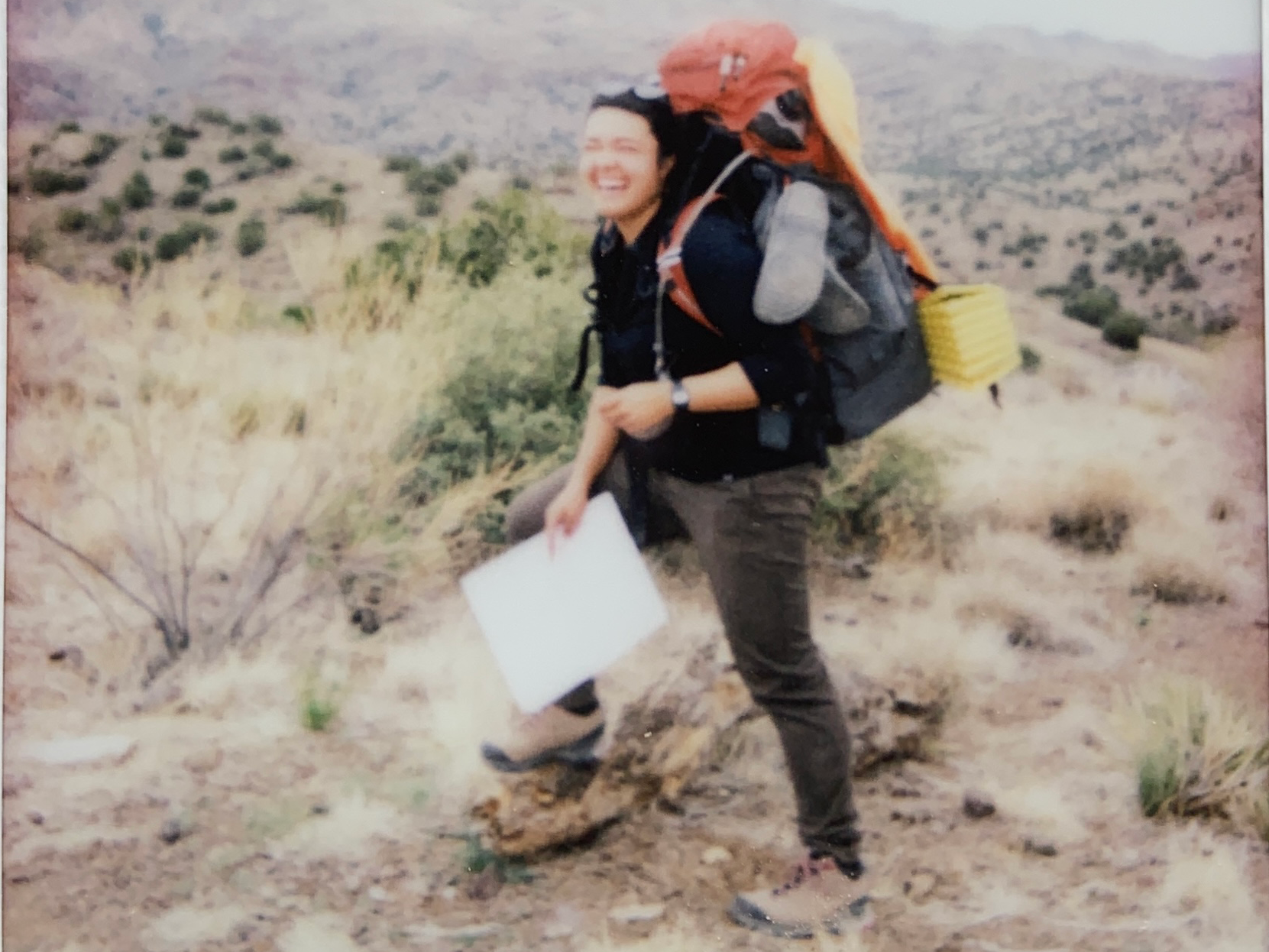 The author is smiling with her backpack on as the holds a map to navigate the desert terrain.
