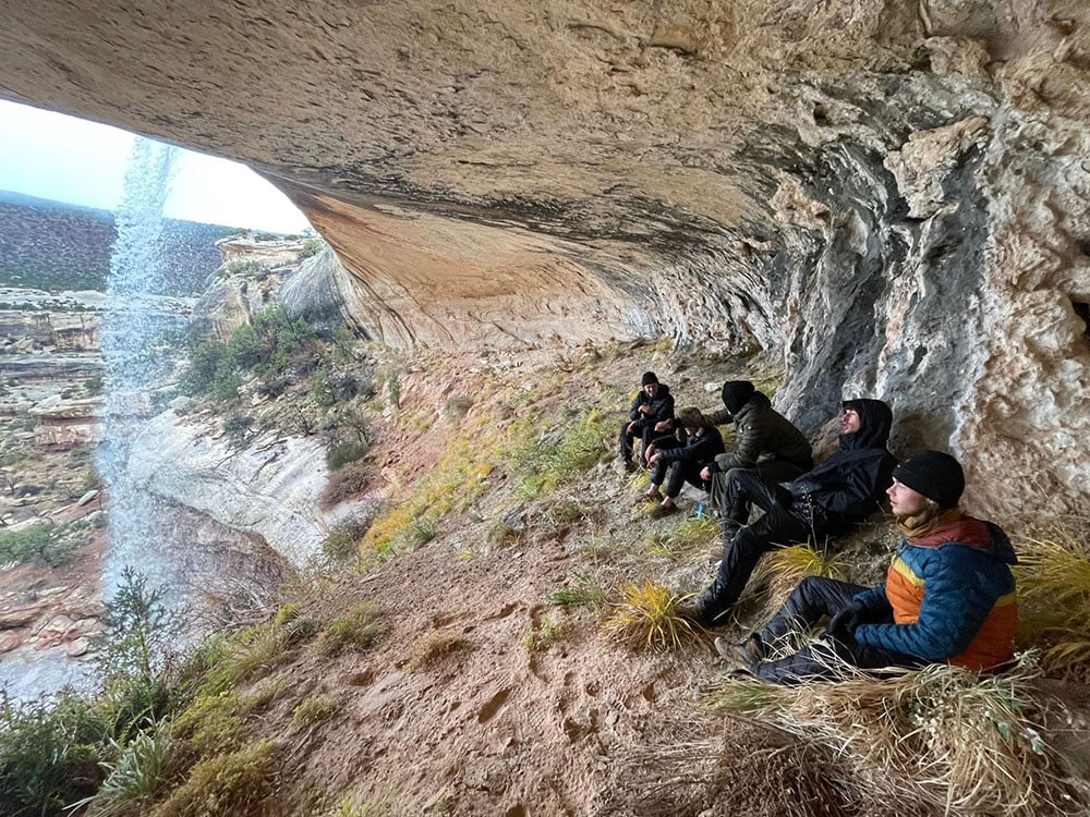 Five students relaxing under a waterfall on a cliff
