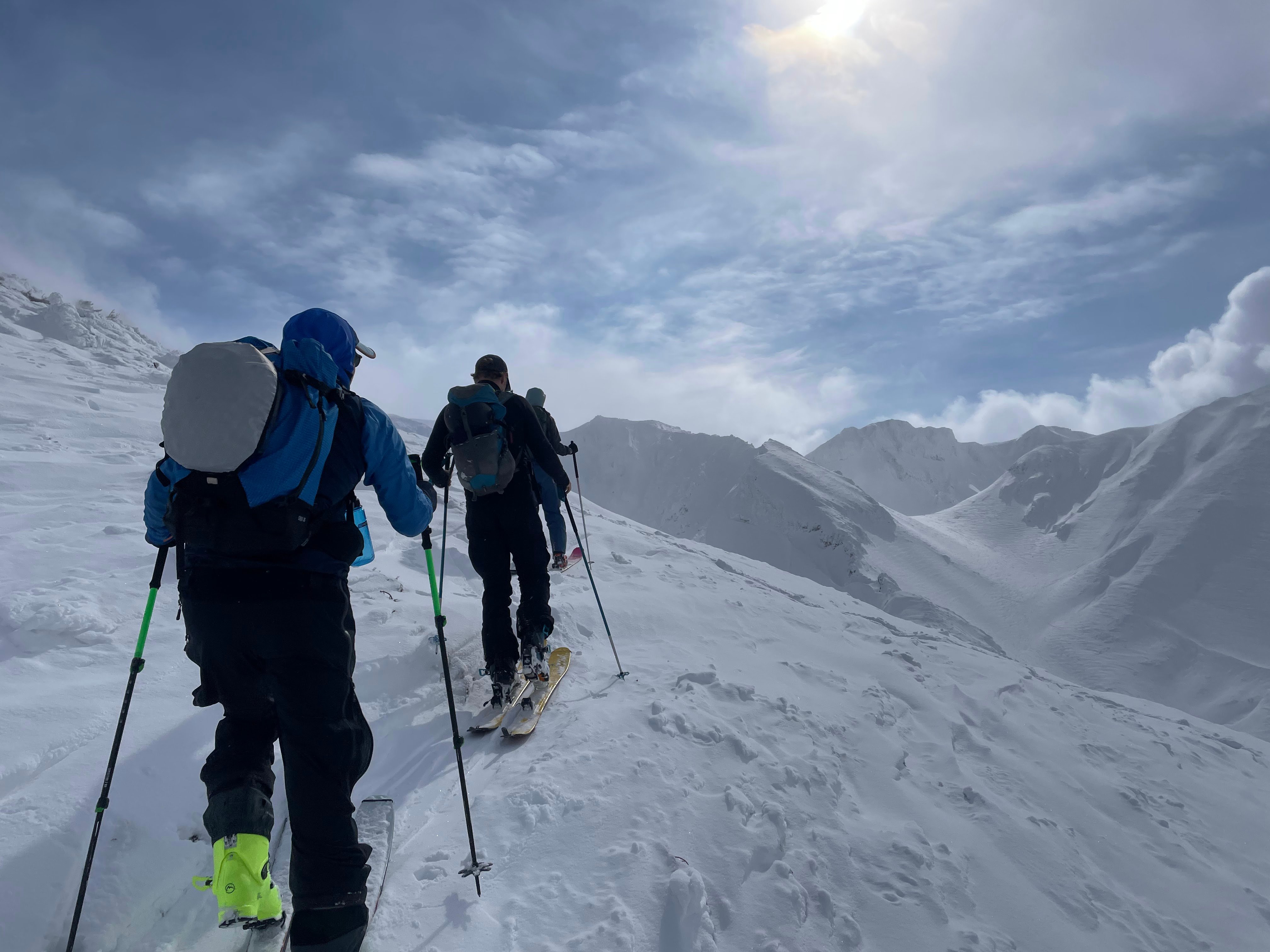 Three skiers moving along a ridge with high, snow-covered mountains close by