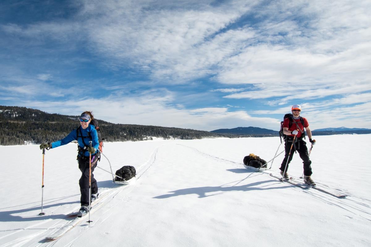 Two people ski touring across an open snow-covered meadow