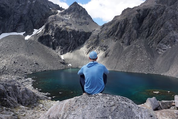 NOLS student sits on a rock overlooking a turquoise alpine lake