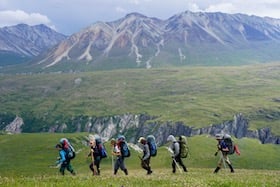 NOLS students hike across a green valley with mountains behind while backpacking in Alaska