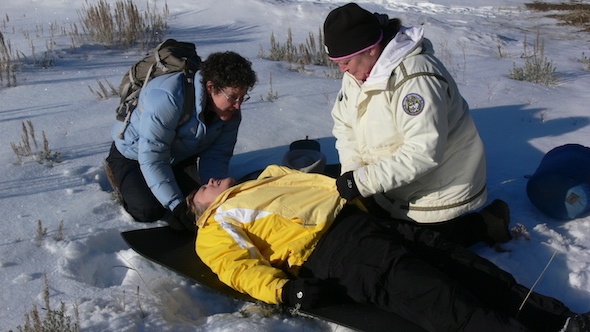 Three NOLS Wilderness Medicine students participate in a scenario in the snow