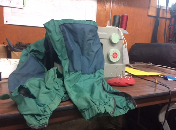 iconic blue and green NOLS windpants draped over a sewing machine awaiting repair