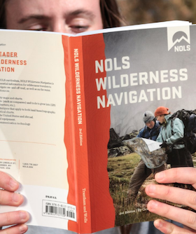 person holds up 3rd edition of NOLS Wilderness Navigation book