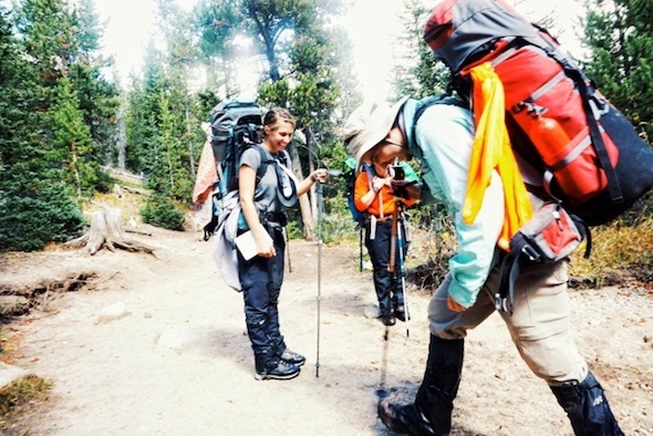 three NOLS participants smile while backpacking, as one hiker squishes water out of his boots