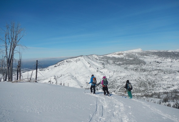 three backcountry skiers on a NOLS course pause at the top of a snowy hill on a sunny day