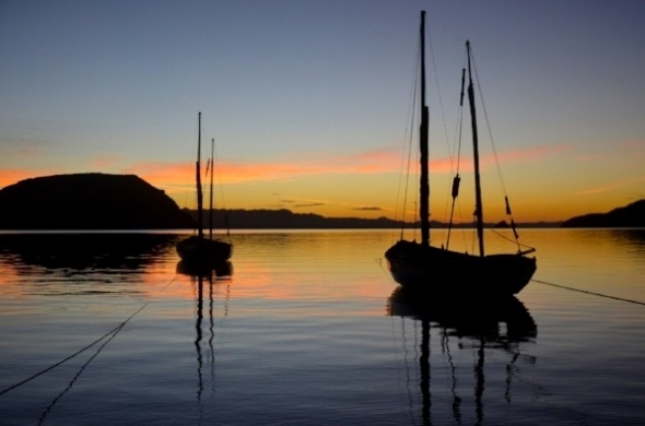 silhouetted sailboats on calm water at sunset in Baja California