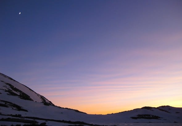 sunset over snowy mountains with crescent moon above