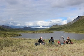 NOLS backpacking students sit beside an alpine lake in Alaska's Talkeetna Mountains