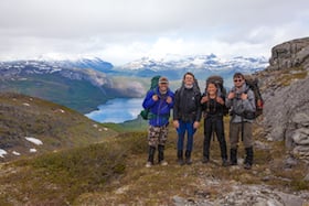 four smiling NOLS students in the Scandinavian mountains with alpine lake