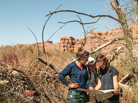 three female NOLS students consult a map with red rocks in the background