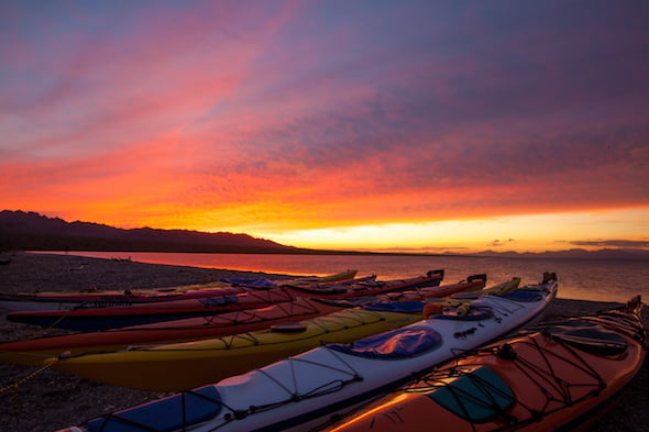 kayaks pulled up on the beach with vivid pink and orange sunset overhead