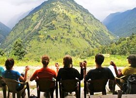 NOLS students sit and drink chai at a teahouse in the Himalaya, looking out at green mountains