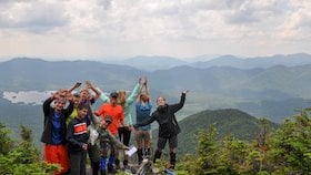 smiling teens with arms outstretched pose for a group photo in the Adirondacks