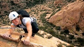 smiling student wearing white helmet rock climbs on red rock