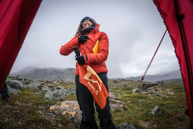 smiling NOLS student in Scandinavia holds NOLS flag in the entrance to a tent