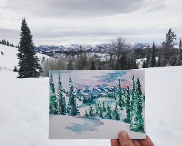 hand holding watercolor of the landscape in the background on a NOLS winter course