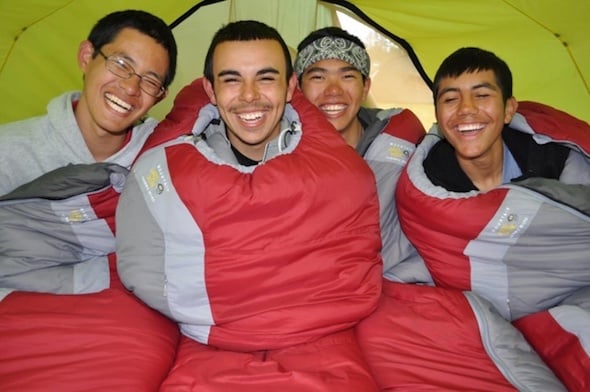 four smiling NOLS students sitting up in their sleeping bags in a tent