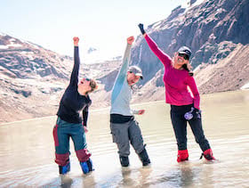 three smiling NOLS students standing in water pump arms in the air victoriously