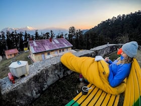 NOLS student wrapped in a sleeping bag journals while looking out at a village in the Himalaya