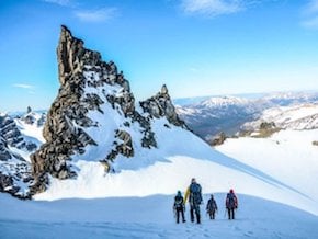 four NOLS participants trek across a snowfield toward a rocky crag in Patagonia's mountains