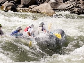 three NOLS participants paddle a raft through a whitewater rapid