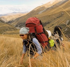 NOLS students hike through tall grass in New Zealand's mountains