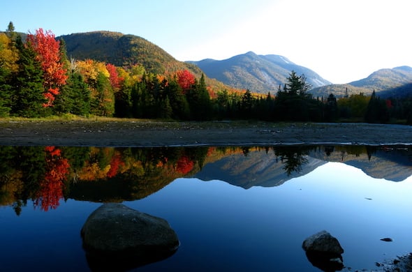 trees with fall colors reflected in a still lake in the mountains