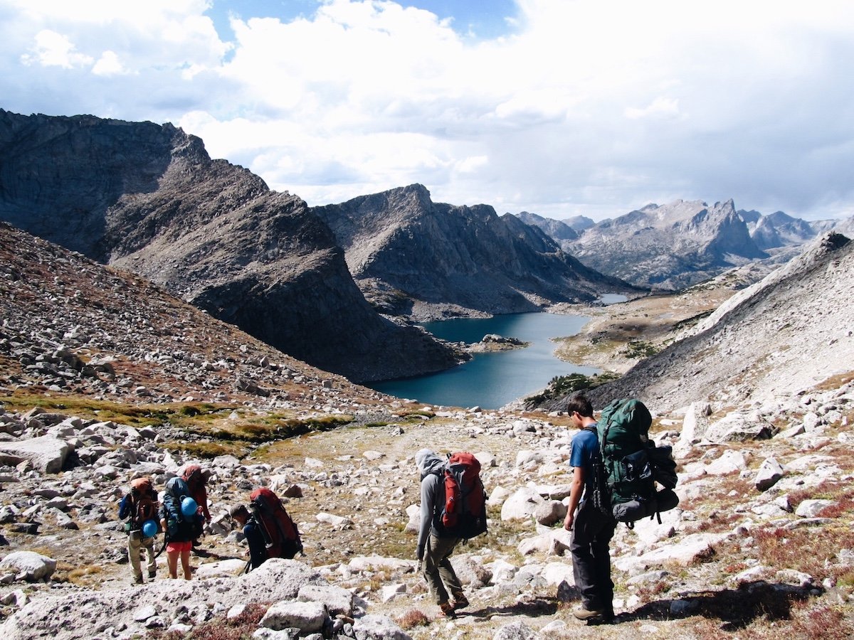 Five NOLS participants hike down rocky slope toward lake in Wyoming's Wind River Range