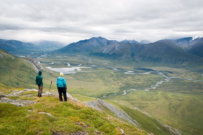 Two people overlook a lush Alaska river valley