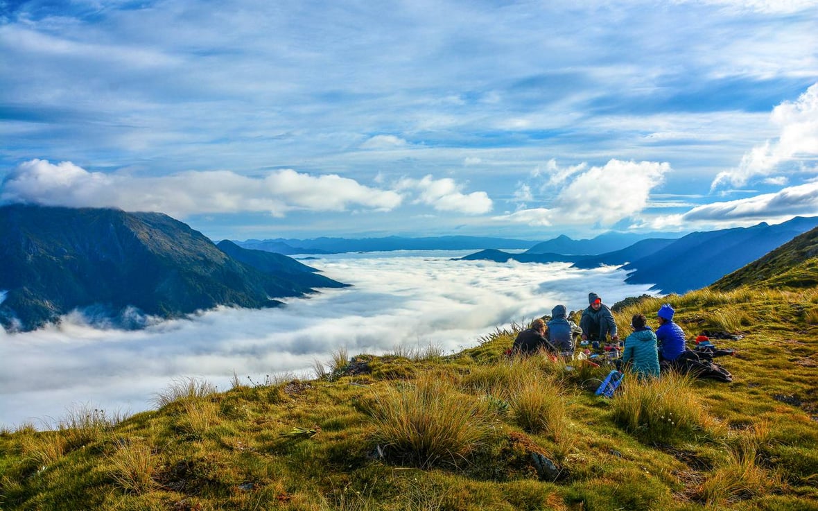 Five students circle up on a grassy knoll in New Zealand with mountains shrouded in clouds