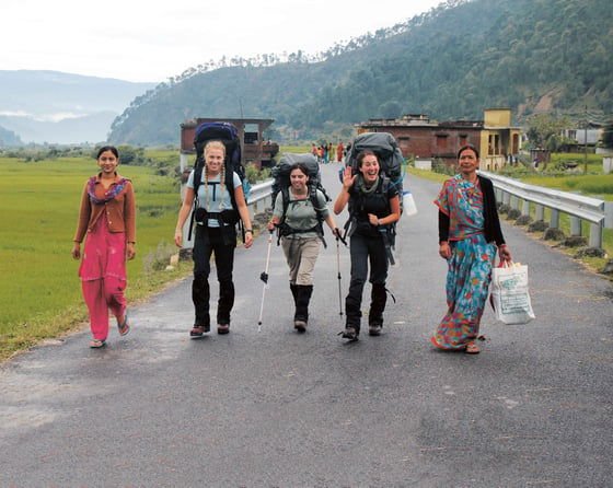 smiling students walk on paved road with local women in the Himalaya