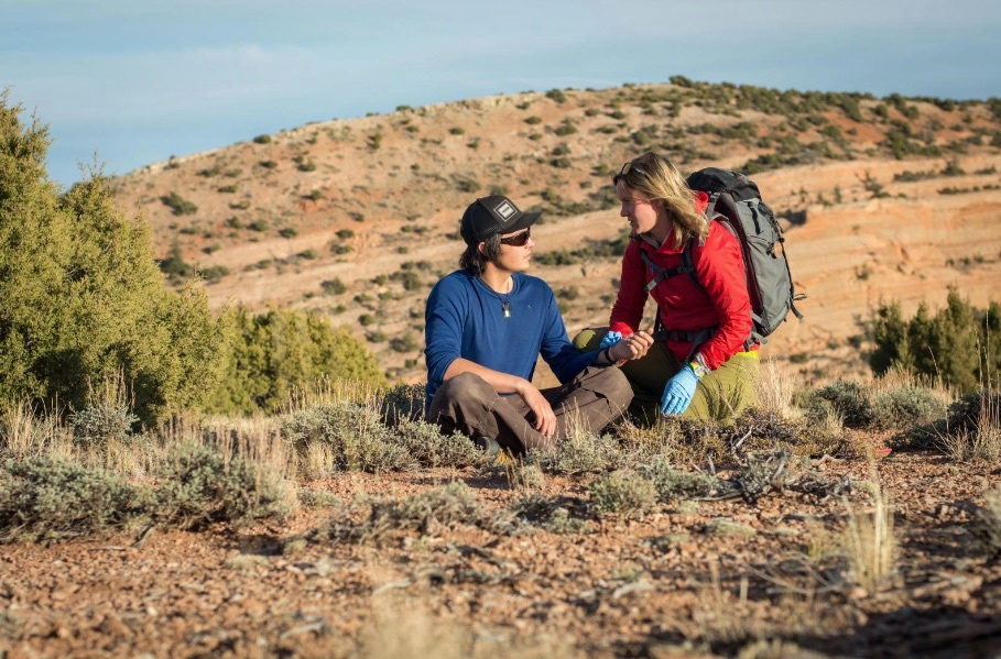 Woman checks the pulse of a man in the outdoors for wilderness first aid