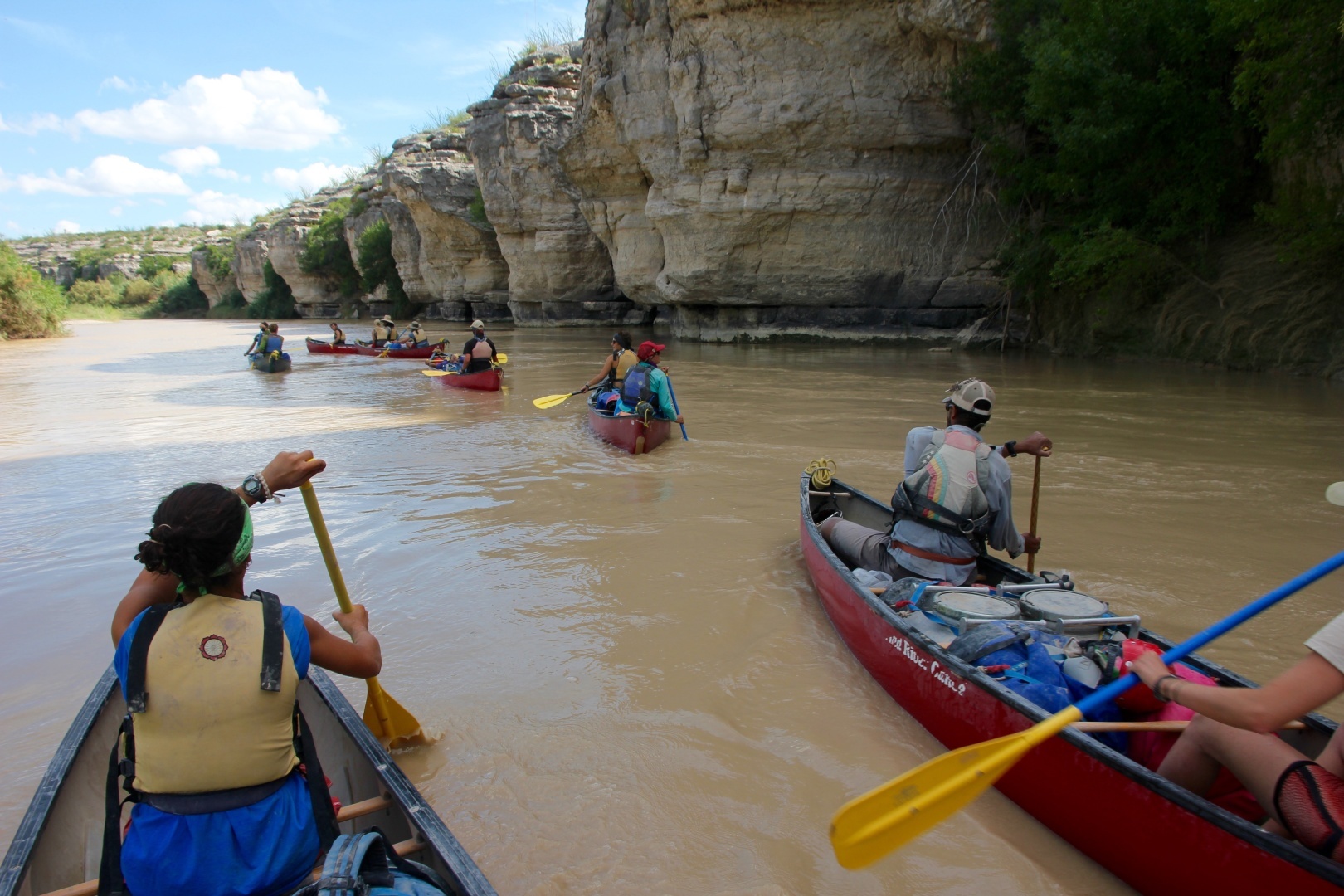 A large group of people canoeing on a river with canyon walls on the right