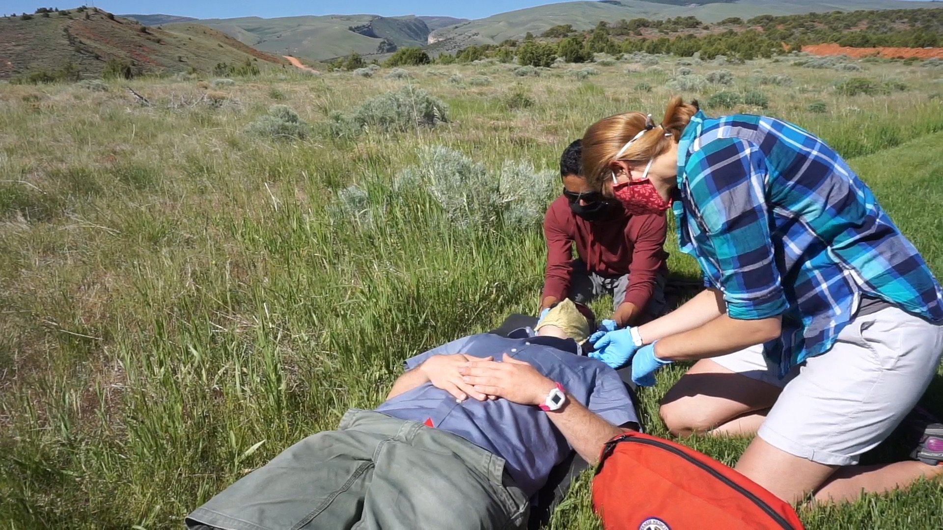 Two people practice attending to a patient in a large grassy field