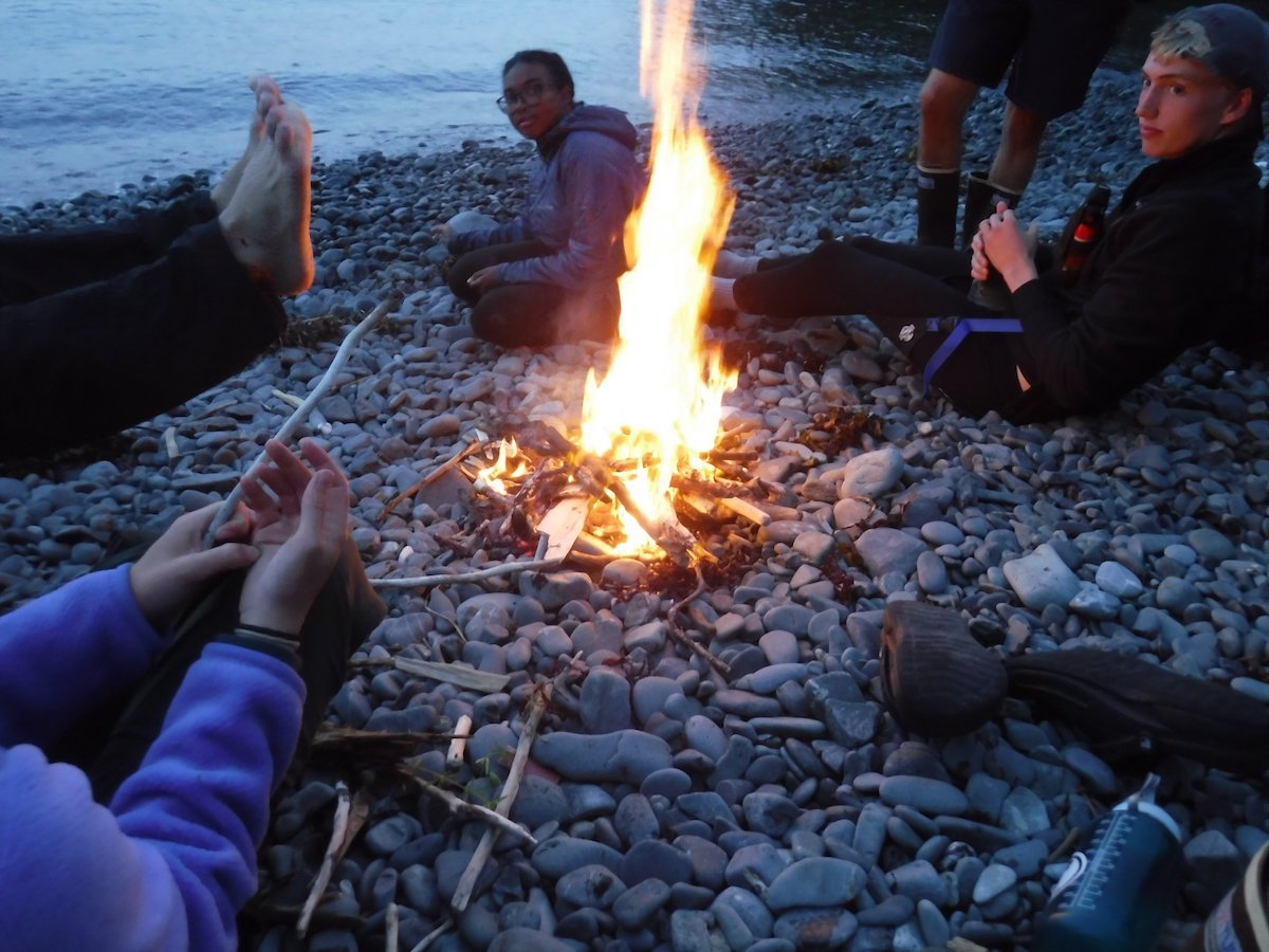 People sitting around a fire on a pebble beach