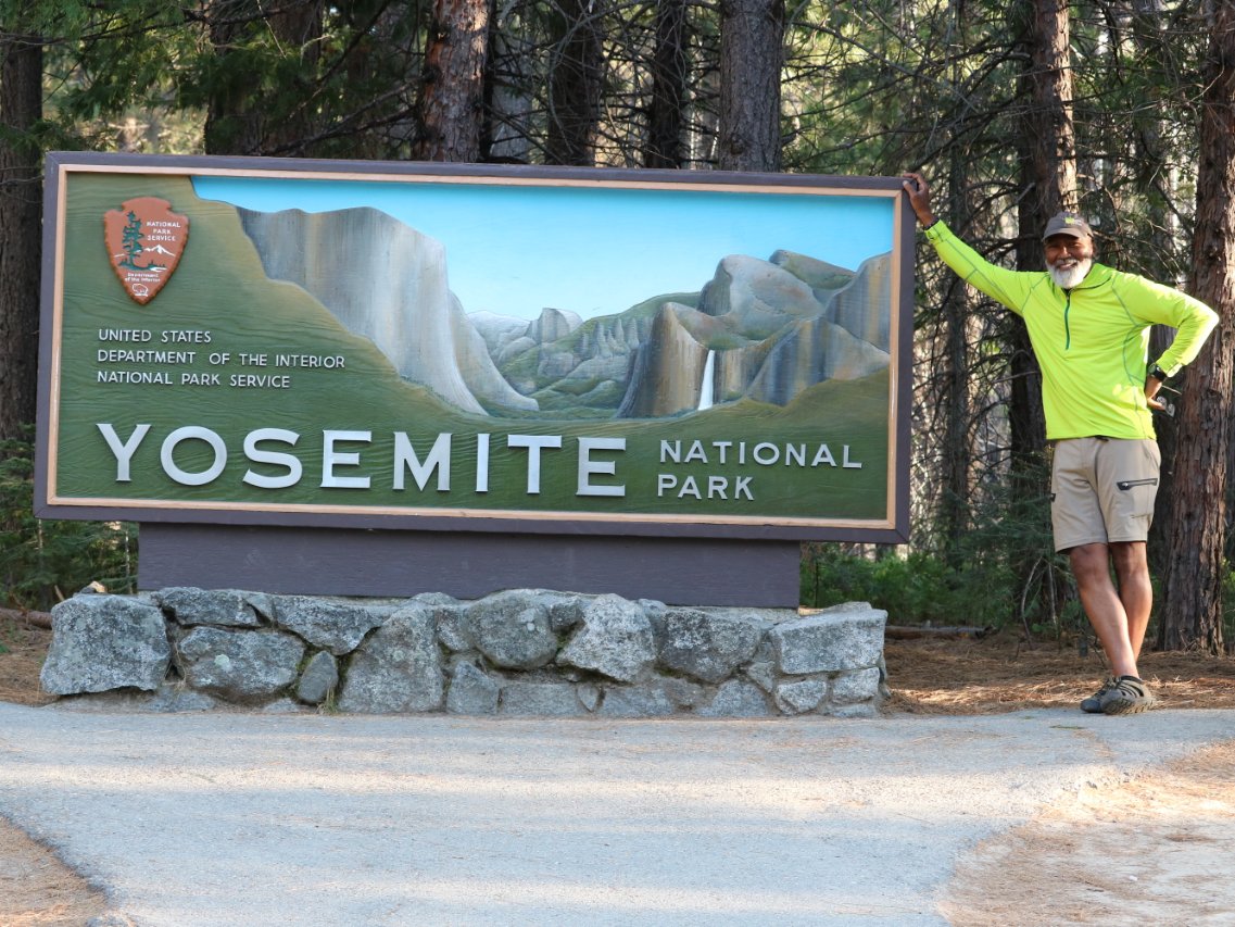Carter McBridge poses at the entrance sign of Yosemite National Park