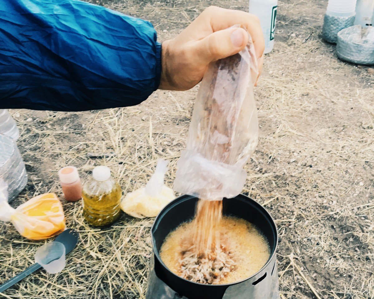 Close up of person pouring a bag of food into a pot on a camp stove